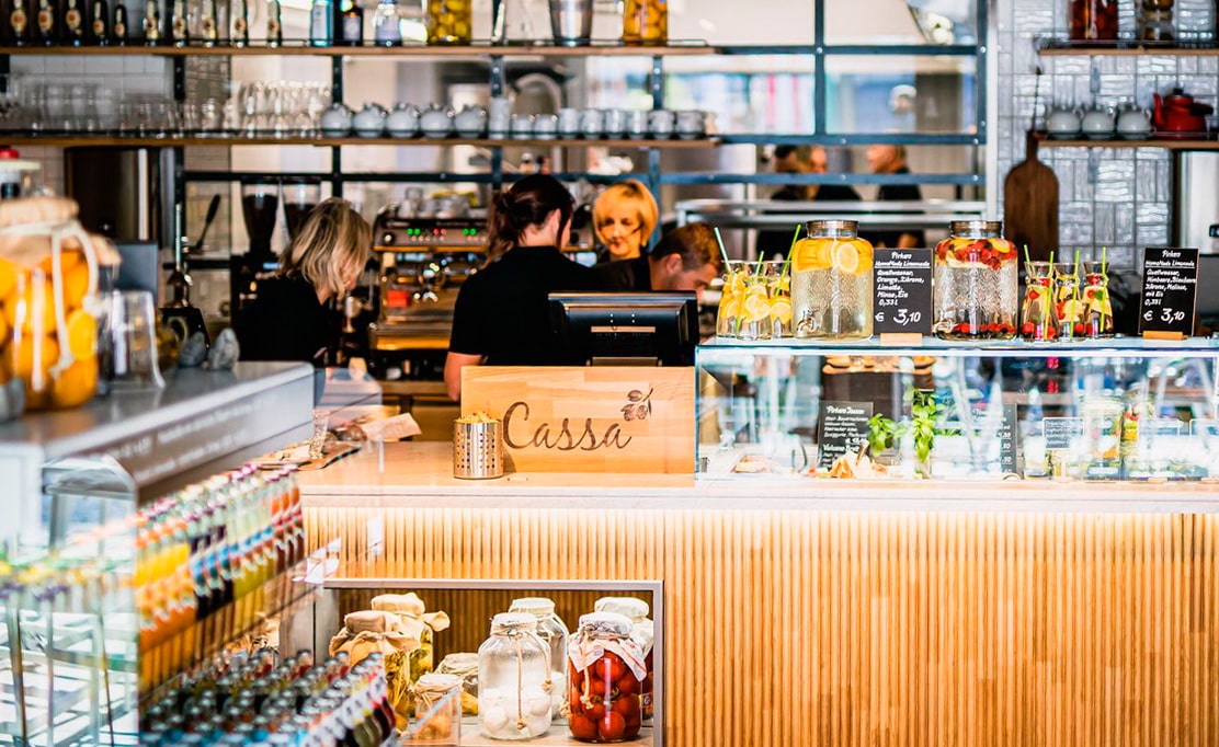 Pirker Bistro Theke mit „Cassa“-Schild, Infused Water in Glasdispensern und Team in der offenen Bar.