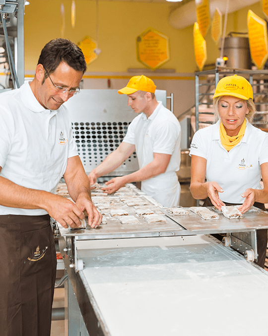 Pirker Lebkuchen Produktion: Frau Pirker und Herr Rippel richten frisch gebackene Stücke an der Förderlinie in der Backstube aus.