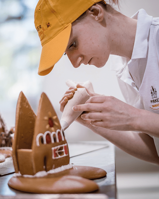 Konditorin verziert Lebkuchenmotiv in der Pirker Lebzelterei – feine Zuckerschrift, Nahaufnahme.