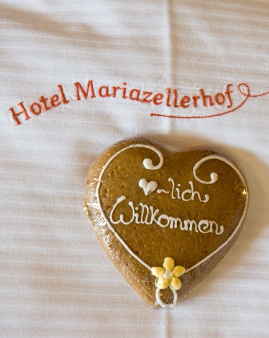 Hotel Mariazellerhof: verpacktes Lebkuchenherz als Willkommensgeschenk auf bestickter Bettwäsche.