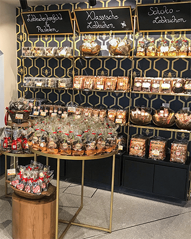 Pirker Lebkuchen Regalwand: klassische, schoko und gefüllte Sorten; runder Tisch mit Geschenkpackungen.