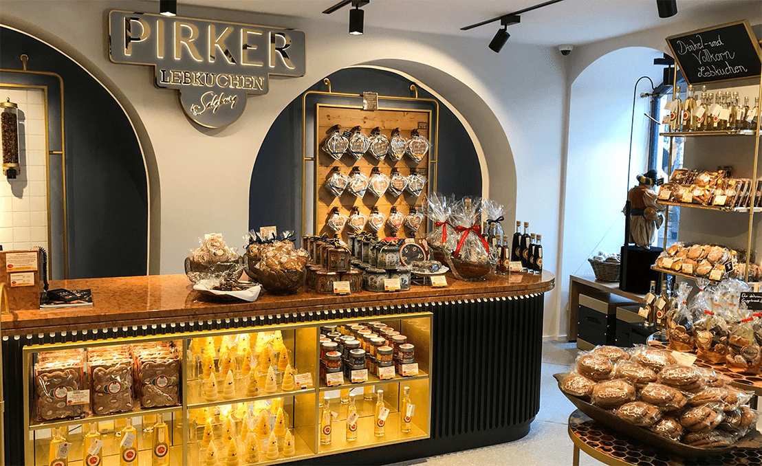 Pirker Lebkuchen – Innenansicht des Shops mit Theke, beleuchteter Vitrine und Wand voller Lebkuchenherzen.