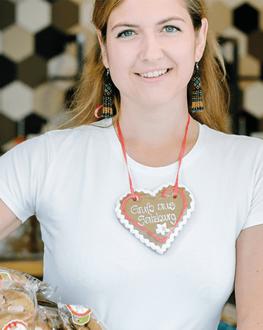 Frau mit Lebkuchenherz „Grüße aus Salzburg“ im Shop – Nahaufnahme mit Gebäck im Vordergrund.