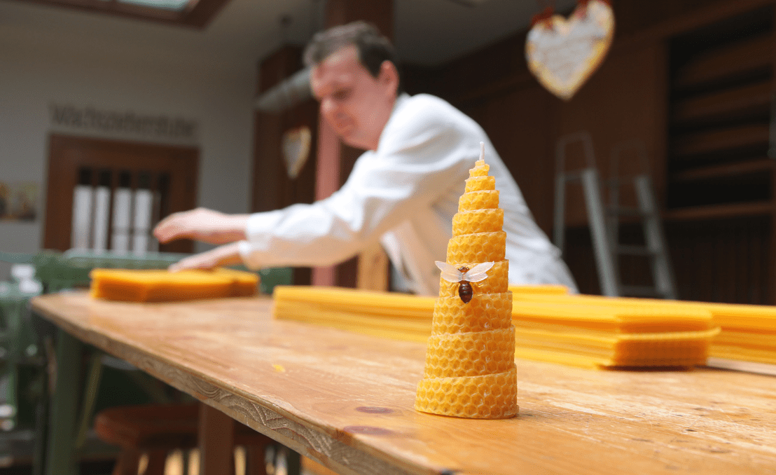 Kerzenwerkstatt Pirker: gerollte Bienenwachskerze mit Deko-Biene, Handarbeit im Hintergrund.
