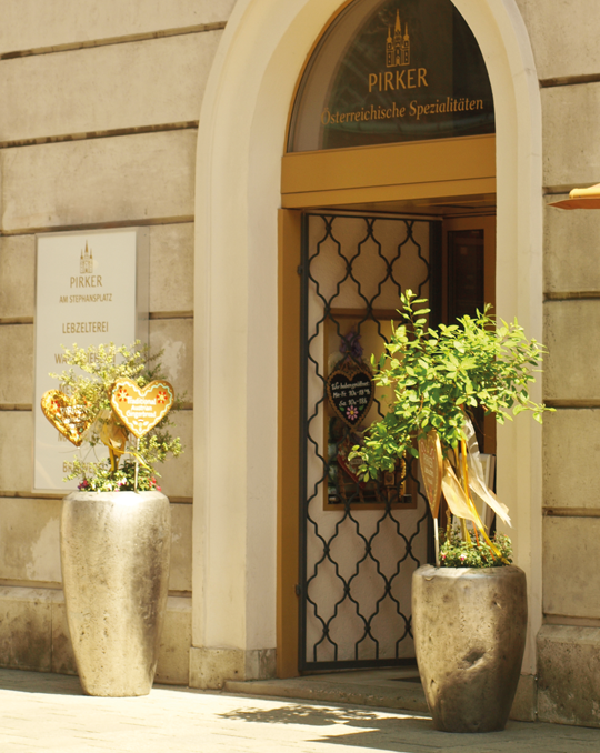 Eingang Pirker am Stephansplatz: Rundbogenportal mit Goldakzenten, zwei Pflanzkübel mit Herzdekor.