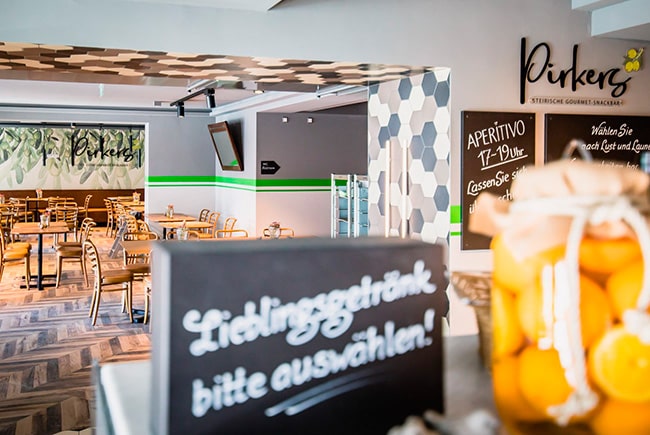 Pirkers Bistro: heller Gastraum mit Holzstühlen, Wandtafel „Aperitivo“ und Bar mit Zitronengläsern.