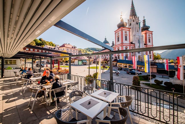 Pirker Terrasse am Hauptplatz Mariazell: Gäste unter Pergola mit Blick auf die Basilika.