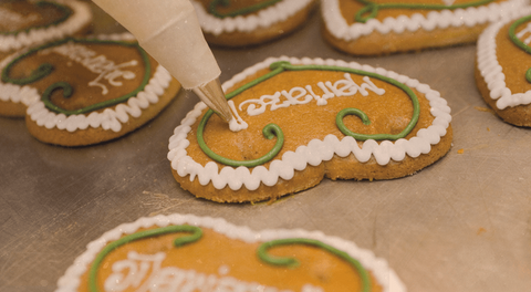 Pirker Lebkuchen: Herz wird mit weißer Zuckerschrift und grüner Bordüre per Spritztüte verziert.