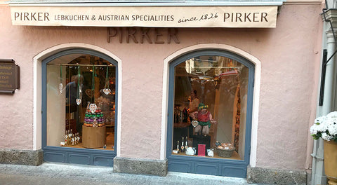 Pirker Lebkuchen Filiale: rosa Fassade mit zwei Rundbogen-Schaufenstern, Auslage mit Lebkuchenherzen und Geschenkboxen.