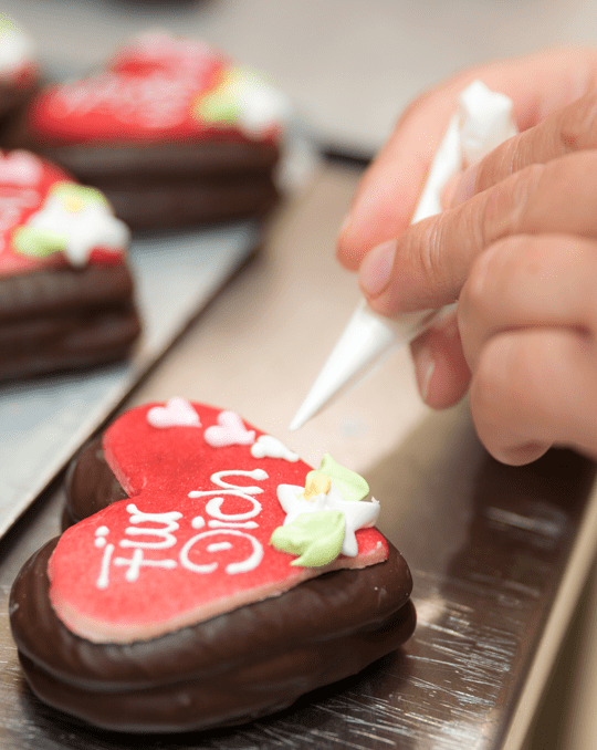 Pirker Lebkuchen: rote Herzlebkuchen mit Schokolade werden per Zuckerschrift verziert.