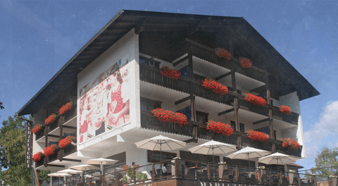 Mariazellerhof: alpines Eckhaus mit Holzbalkonen, roten Geranien und großer Sonnenterrasse
